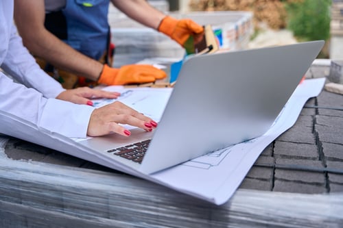 Person using a laptop on roofing plans while discussing costs and the question is roofing business profitable.