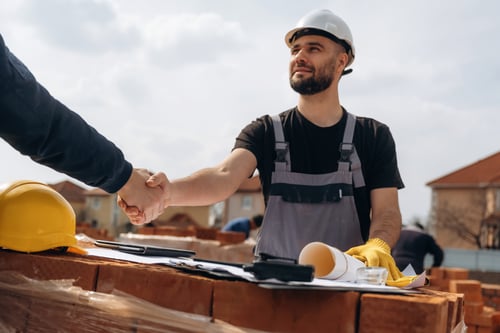 Roofer shaking hands on a construction site deal while discussing the question is roofing business profitable.
